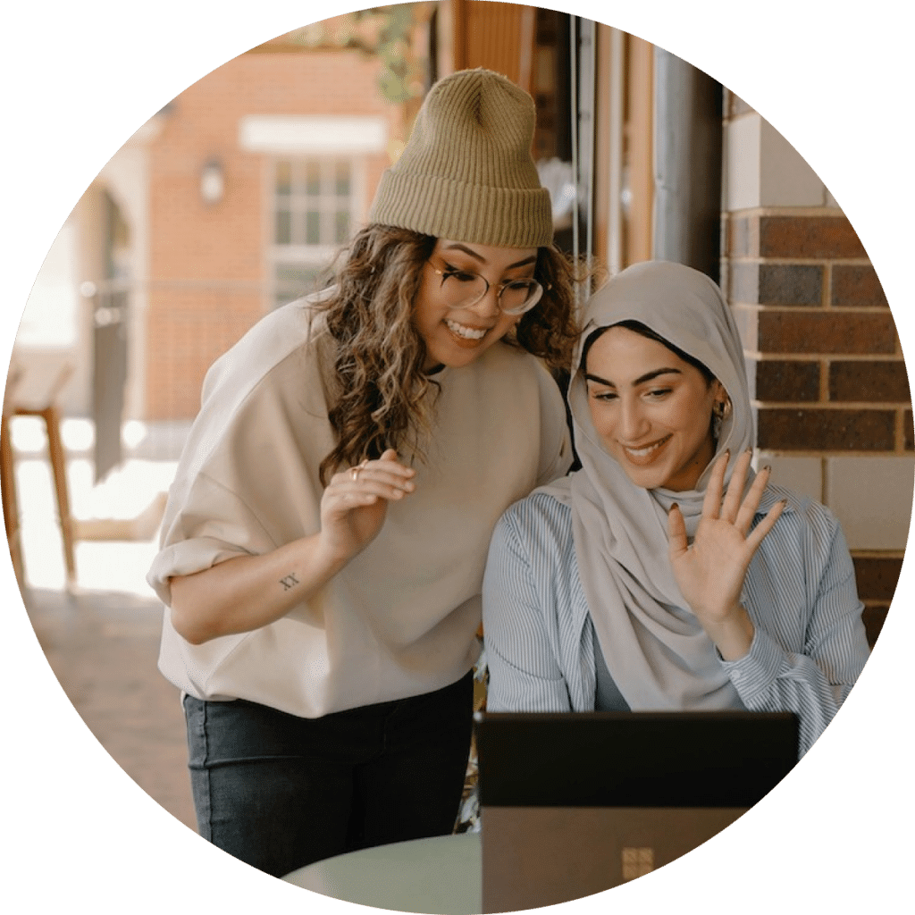 two girls working on a laptop together waving their hand